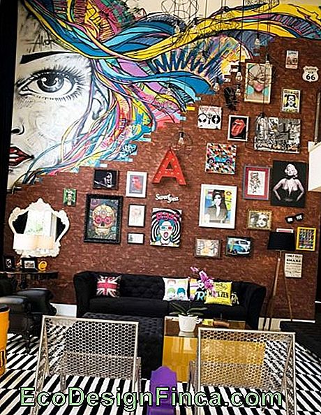 Image d'une pièce avec un mur de briques où se trouvent plusieurs images. Au sommet du mur, il tombe en morceaux et donne lieu aux graffitis sur le visage d'une femme aux cheveux colorés.