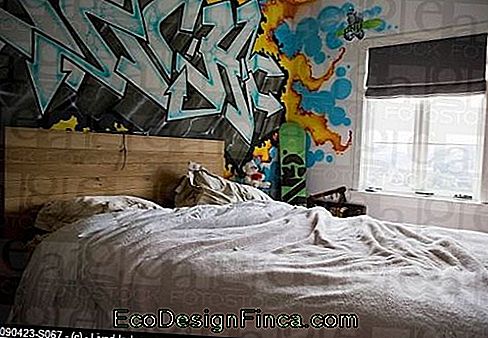 Image d'un lit avec une tête de palettes et le mur derrière tout décoré de graffitis, principalement des lettres.